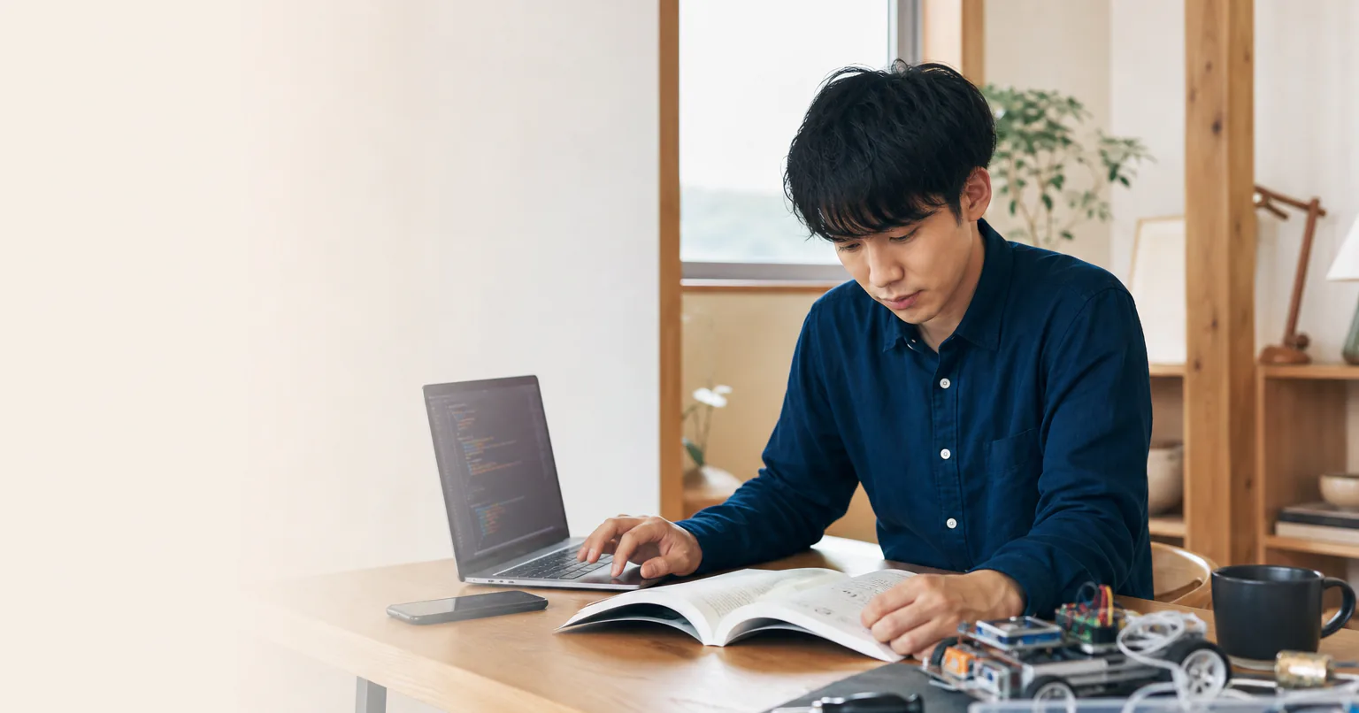 教材、ノートパソコン、スマートフォン、小型電子部品を並べて学ぶ内容を整理する受講者